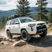 White SUV driving on a rocky trail with trees and mountains in the background