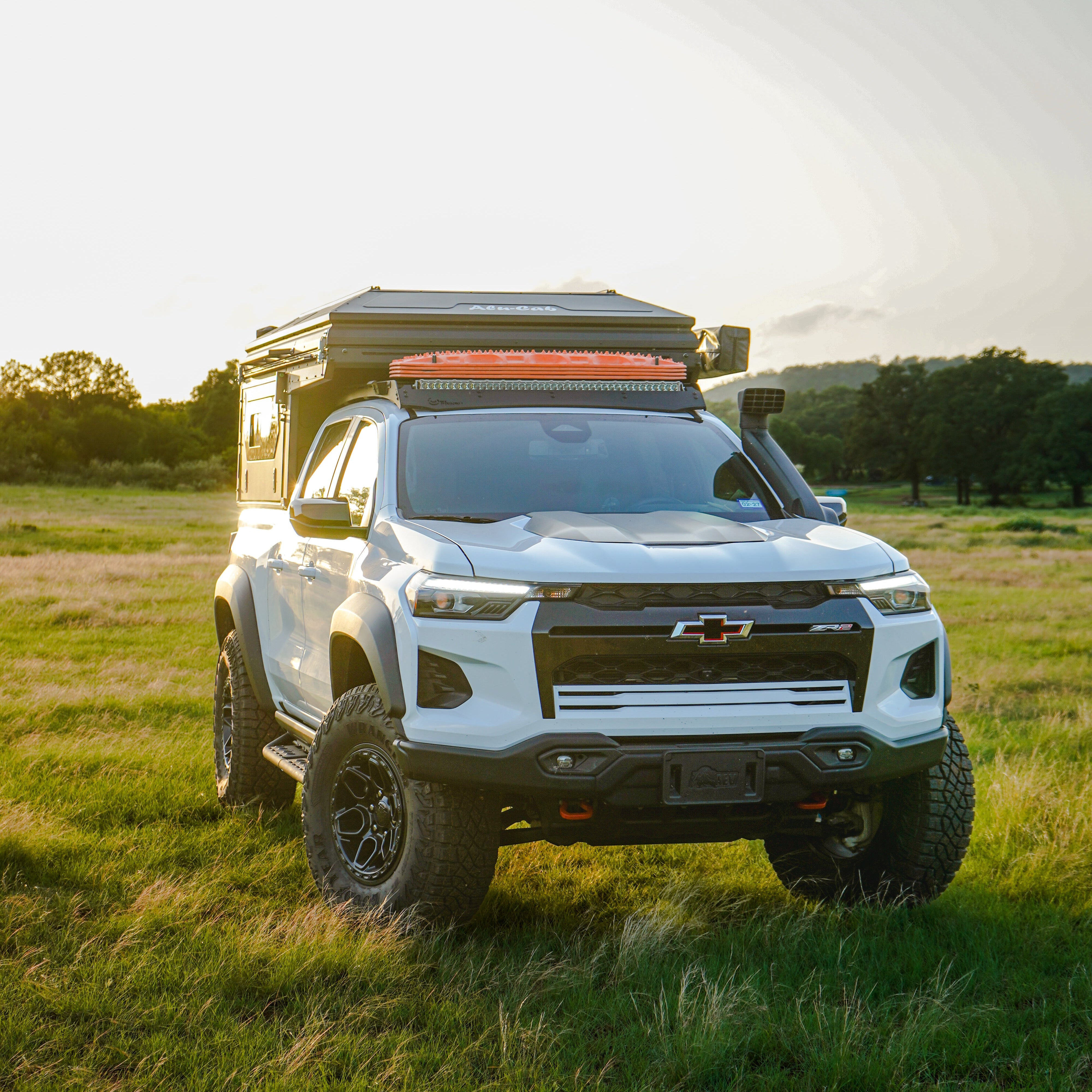 White SUV with a camper shell parked in a grassy field during sunset.